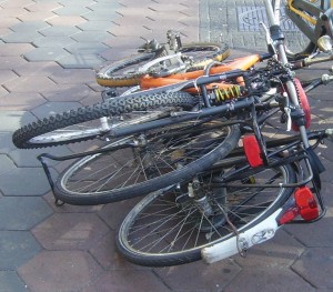 The image shows a few bicycles that have fallen over and are lying on a paved surface. The bicycles are tangled together, with their wheels and frames overlapping. The pavement consists of hexagonal tiles.