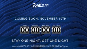 The image is a promotional advertisement for Radisson. It features a blue background with wavy patterns and the Radisson logo at the top. The text reads "COMING SOON, NOVEMBER 10TH" followed by a countdown timer showing "00 DAYS 00 HOURS 00 MINUTES 00 SECONDS." Below the timer, the text says "STAY ONE NIGHT, GET ONE NIGHT!" At the bottom, there is additional text that reads, "To celebrate the U.S. debut of Radisson Blu, we're giving away up to 50,000 nights. Hurry — offer is limited to the first 50,000 guests that register."