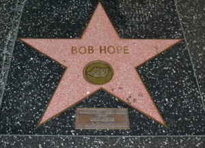 The image shows a star on the Hollywood Walk of Fame with the name "Bob Hope" inscribed on it. The star is pink with a bronze film camera emblem in the center, set in a black terrazzo background. There is also a small plaque below the star.