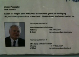 The image shows a notice with contact information for passengers. The text is in both German and English. It reads:

"Lieber Passagier,
Dear Guests,
haben Sie Fragen oder Kritik? Wir stehen Ihnen gerne zur Verfügung.
do you have any questions or feedback? Please do not hesitate to contact us.

Ihr Ansprechpartner ist:
Herr Hans-Ulrich Schröter
Telefon: 069 690-2091
E-Mail: hans.schroeter@fraport.de

Your contact person is:
Mr. Hans-Ulrich Schröter
Phone: +49 69 690-2091
E-Mail: hans.schroeter@fraport.de"

There is also a small photograph of a man, presumably Mr. Hans-Ulrich Schröter, in the bottom left corner of the notice.