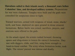 The image contains a block of text describing the military systems and warfare of ancient Hawaiians. It explains that Hawaiians sailed to their islands nearly a thousand years before Columbus' time and developed elaborate preparations for war, including building temples and consulting gods for auspicious times to fight. The text details the warriors' weapons made of wood, stone, sharks' teeth, and bone, and their deployment in crescent formations. It also describes the rituals of sacrifices, prayers, and orations before battle. The text further narrates the intensity and brutality of the combat, with armies throwing spears and sling-stones, and engaging in hand-to-hand combat with daggers, clubs, and fists. The passage concludes by mentioning the victors' pursuit after the enemy's formation broke.