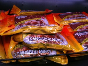 The image shows several packages of kangaroo mince meat on a store shelf. The packaging is predominantly yellow and orange, with the text "Kangaroo Mince" clearly visible on the front of each package. The packages are stacked on top of each other.