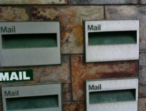 The image shows four mail slots on a brick wall. Each slot is labeled "Mail" and has a rectangular opening for inserting letters. The slots are arranged in a grid pattern, with two on the top row and two on the bottom row. The background consists of a brick wall with a mix of brown and gray tones.