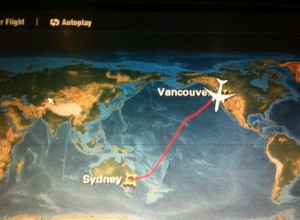 A world map showing a flight path from Sydney, Australia to Vancouver, Canada. The path is marked with a red line, and there is an airplane icon near Vancouver. The map includes labels for both cities.