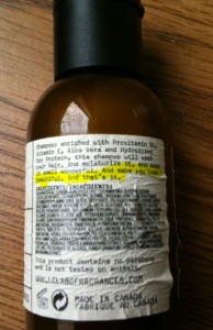 The image shows a brown bottle with a black cap, placed on a wooden surface. The bottle has a label with text detailing the product's ingredients and usage instructions. The text on the label is small and includes highlighted sections. The label mentions that the product is a shampoo enriched with various ingredients such as Previntain, Aloe Vera, and Hydrolyzed Soy Protein. The highlighted text reads, "And make you look younger. And that is no." The bottom of the label indicates that the product is made in Canada.