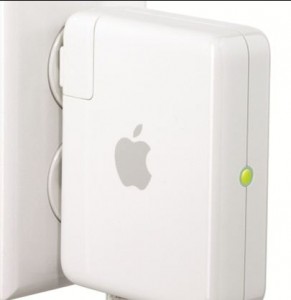 The image shows a white Apple device plugged into a wall outlet. The device has the Apple logo on it and a small green indicator light on the side.