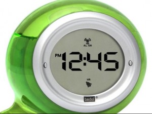 The image shows a digital clock with a green, rounded casing. The display reads "12:45 PM" and has icons indicating that the alarm is on. The brand name "bedol" is visible at the bottom of the display.