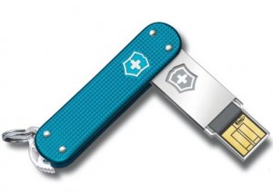 The image shows a blue Swiss Army knife with a built-in USB flash drive. The USB drive is extended out from the knife, revealing the connector. The knife has a keyring attached to one end and features the Swiss Army logo on both the knife handle and the USB drive.