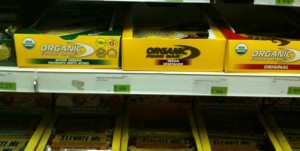 The image shows a supermarket shelf with three different types of organic food bars. The boxes are labeled "Organic Food Bar" and come in different varieties: "Active Greens," "Protein," and "Original." The price tags are visible below each box on the shelf. The shelf below also contains more boxes of food bars.