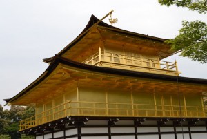 The image shows a traditional Japanese building with golden walls and a multi-tiered roof. The structure is known as Kinkaku-ji, or the Golden Pavilion, located in Kyoto, Japan. The building is surrounded by trees and has a serene, peaceful atmosphere.