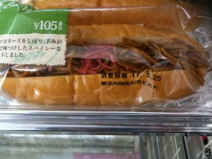 The image shows a packaged sandwich with a price tag of ¥105. The sandwich appears to contain yakisoba (Japanese stir-fried noodles) and some pickled ginger. The packaging has some text in Japanese, including an expiration date of 11.5.25. The sandwich is displayed on a shelf, likely in a convenience store or supermarket.