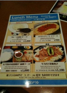 The image is of a lunch menu from a restaurant. The menu is divided into four sections, each displaying a different dish with a picture, description, and price. The dishes include:

1. A plate of curry with rice, priced at ¥1,000.
2. Spaghetti with meat sauce, priced at ¥950.
3. A set meal with a main dish, rice, and soup, priced at ¥1,000.
4. A beef dish with vegetables, priced at ¥1,100.

The menu also mentions that coffee or tea can be added for an additional ¥100. The menu is in both Japanese and English, and it is for weekdays and holidays from 11:30 to 15:00.