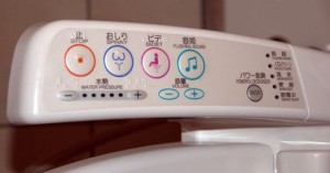 The image shows the control panel of a Japanese bidet toilet seat. The panel includes various buttons and icons for different functions such as water pressure adjustment, bidet spray, and flushing sound. The buttons are labeled in Japanese and have corresponding icons, including a water droplet, a person, and musical notes. There are also plus and minus buttons for adjusting settings.