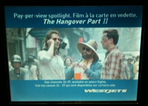 The image is an advertisement for the movie "The Hangover Part II" on a pay-per-view spotlight. The ad features a scene from the movie with three men standing together, one of whom is wearing a hat and sunglasses. The text on the ad is in both English and French, indicating that the movie is available on select flights on channels 26-29. The WestJet logo is visible at the bottom of the ad.