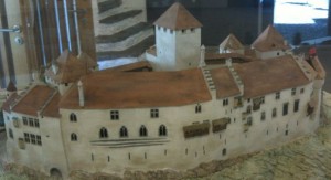 A detailed model of a medieval castle with multiple towers and a large central keep. The castle has a brown roof and white walls with several windows and small balconies. The model is displayed indoors, possibly in a museum or exhibition setting.