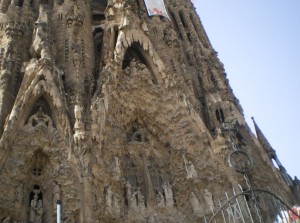 The image shows a close-up view of the intricate and detailed facade of the Sagrada Família, a famous basilica in Barcelona, Spain. The architecture features numerous sculptures, carvings, and ornate designs, showcasing the unique and elaborate style of the building. The sky is clear and blue in the background.