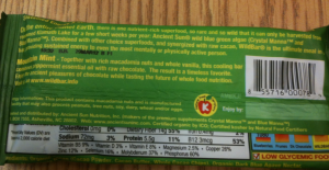 The image shows the back of a green packaged food product, specifically a chocolate bar. The packaging includes a description of the product, nutritional information, and a barcode. The text describes the product as a nutrient-rich superfood with ingredients like macadamia nuts, wild peppermint, and raw cacao. The nutritional information includes details on calories, fat, sodium, carbohydrates, fiber, sugars, protein, vitamins, and minerals. There are also various certifications and labels indicating the product is organic, gluten-free, and low glycemic.