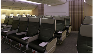 The image shows the interior of an airplane cabin, specifically the economy class section. The seats are arranged in rows, with each seat having a headrest and armrests. The seats are upholstered in dark and light-colored materials, and there are small screens or trays on the back of each seat. The cabin is well-lit, and the overhead compartments are closed. The overall appearance is clean and modern.